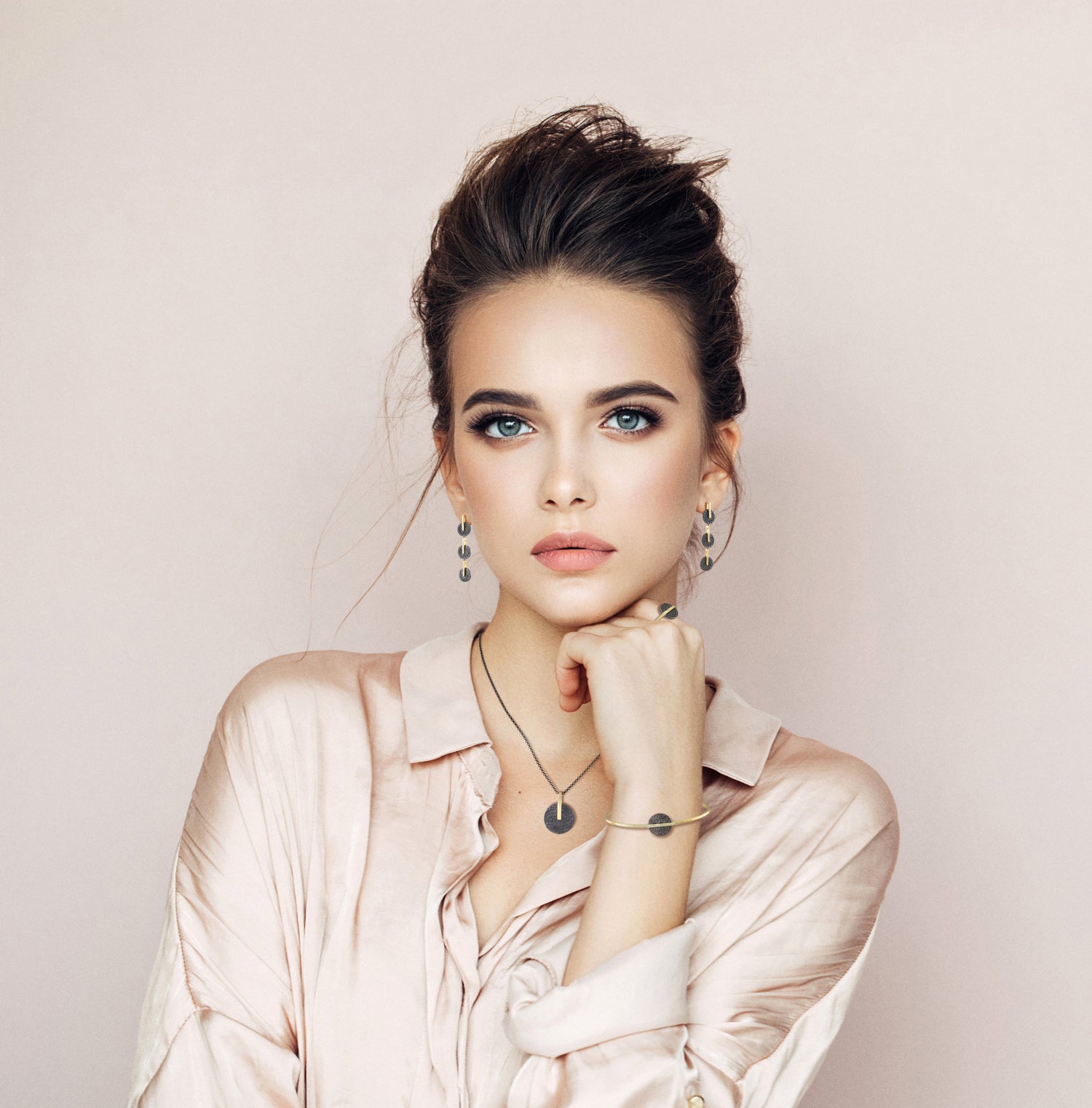 Black and gold tone designer jewellery by Spanish artist Jorge Revilla modelled by beautiful dark haired woman wearing a neutral coloured satin shirt