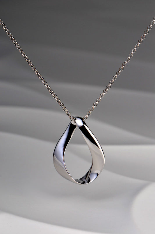 Modern polished sterling silver pendant in a twisted ribbon design that forms a droplet shape with a space in the middle. Like a teardrop shape. This necklace is by Jorge Revilla