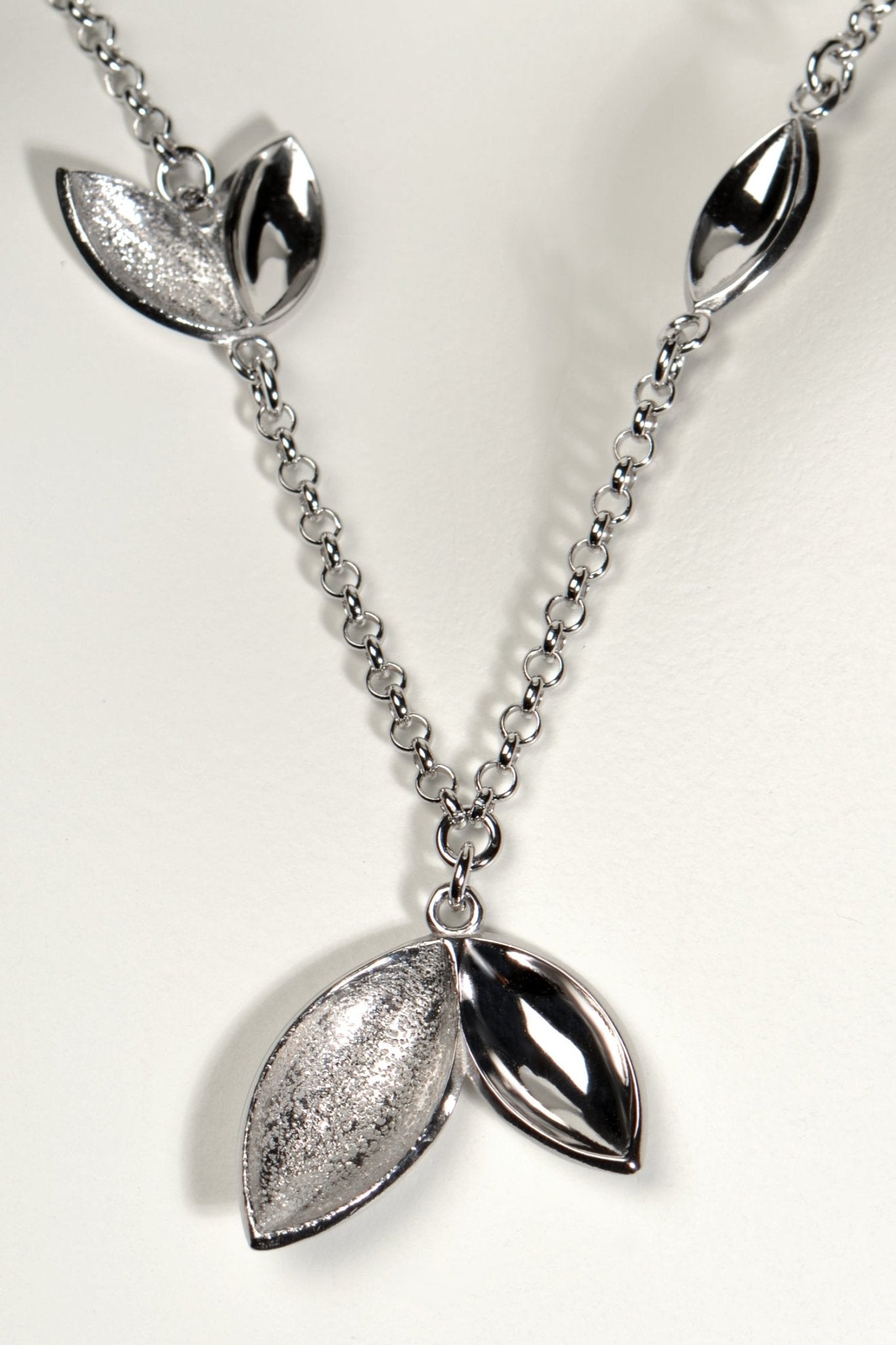 modern silver charm necklace with concave seed like shapes in highly polished silver and modern textured finishes. Called The Promise, a tree is planted for each one of these necklaces sold by Christine Sadler