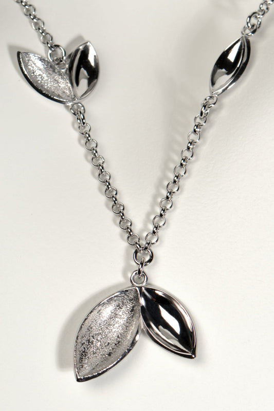 modern silver charm necklace with concave seed like shapes in highly polished silver and modern textured finishes. Called The Promise, a tree is planted for each one of these necklaces sold by Christine Sadler