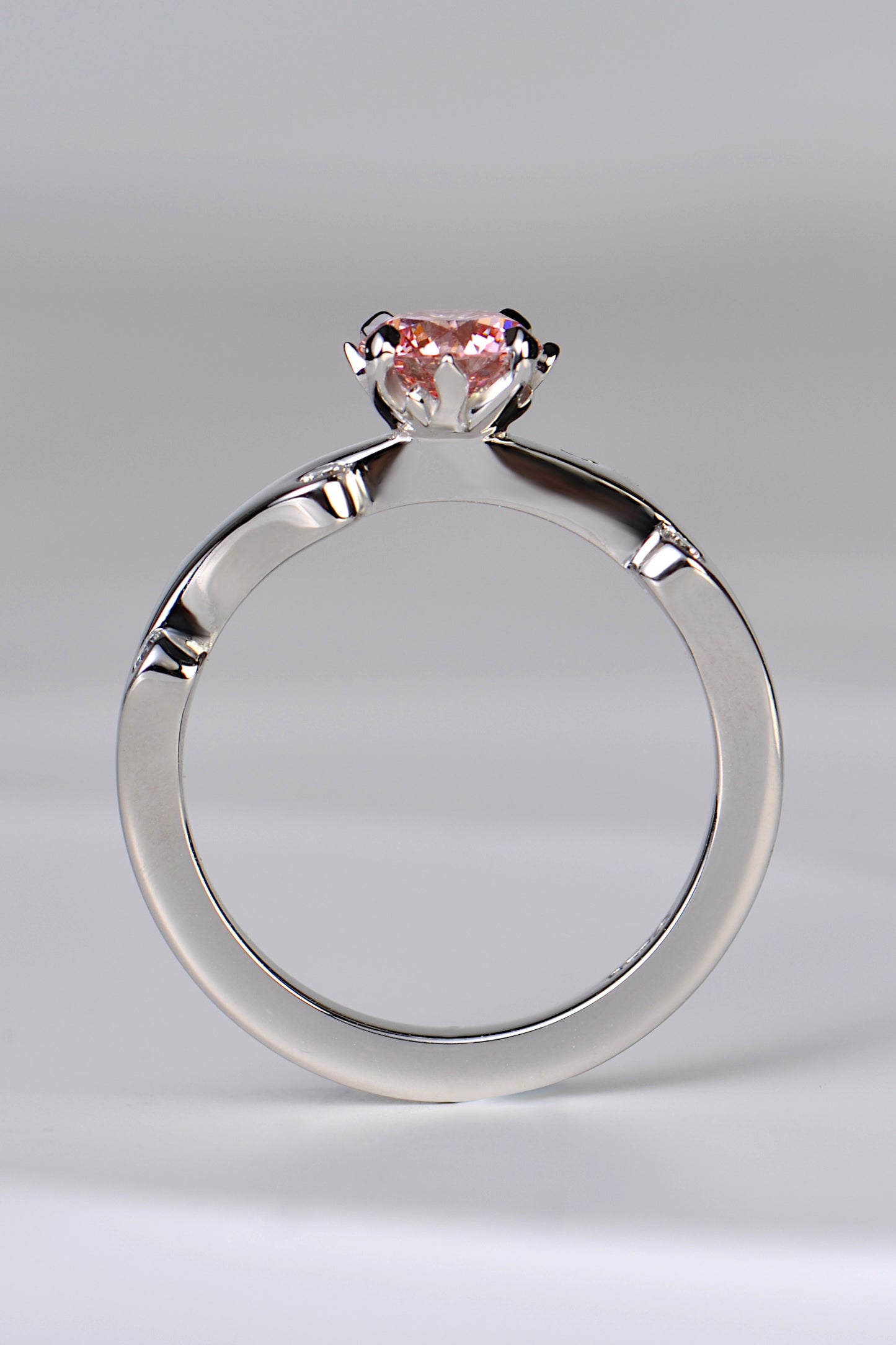 A platinum engagement ring set with a large round pink lab diamond in rose pink shade. The diamond is held in a setting that looks like tiny flames are surrounding it. A unique and special diamond ring design by jewellery designer Christine Sadler.