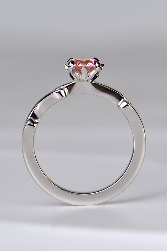 A platinum engagement ring set with a large round pink lab diamond in rose pink shade. The diamond is held in a setting that looks like tiny flames are surrounding it. A unique and special diamond ring design by jewellery designer Christine Sadler.