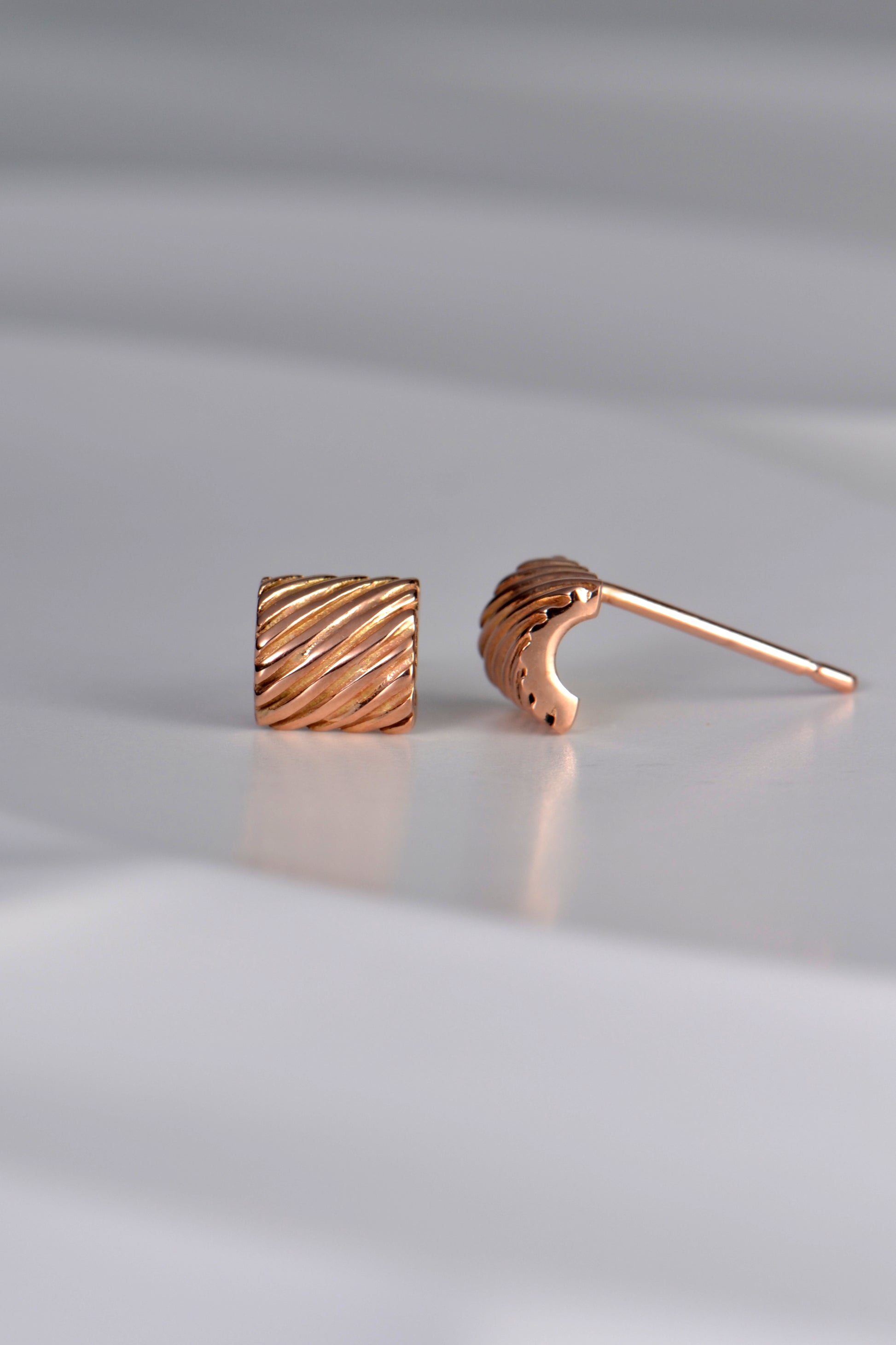 modern reectangular small rose gold stud earring. The rectangular shape curves and the earring posts sits at the top of the stud.