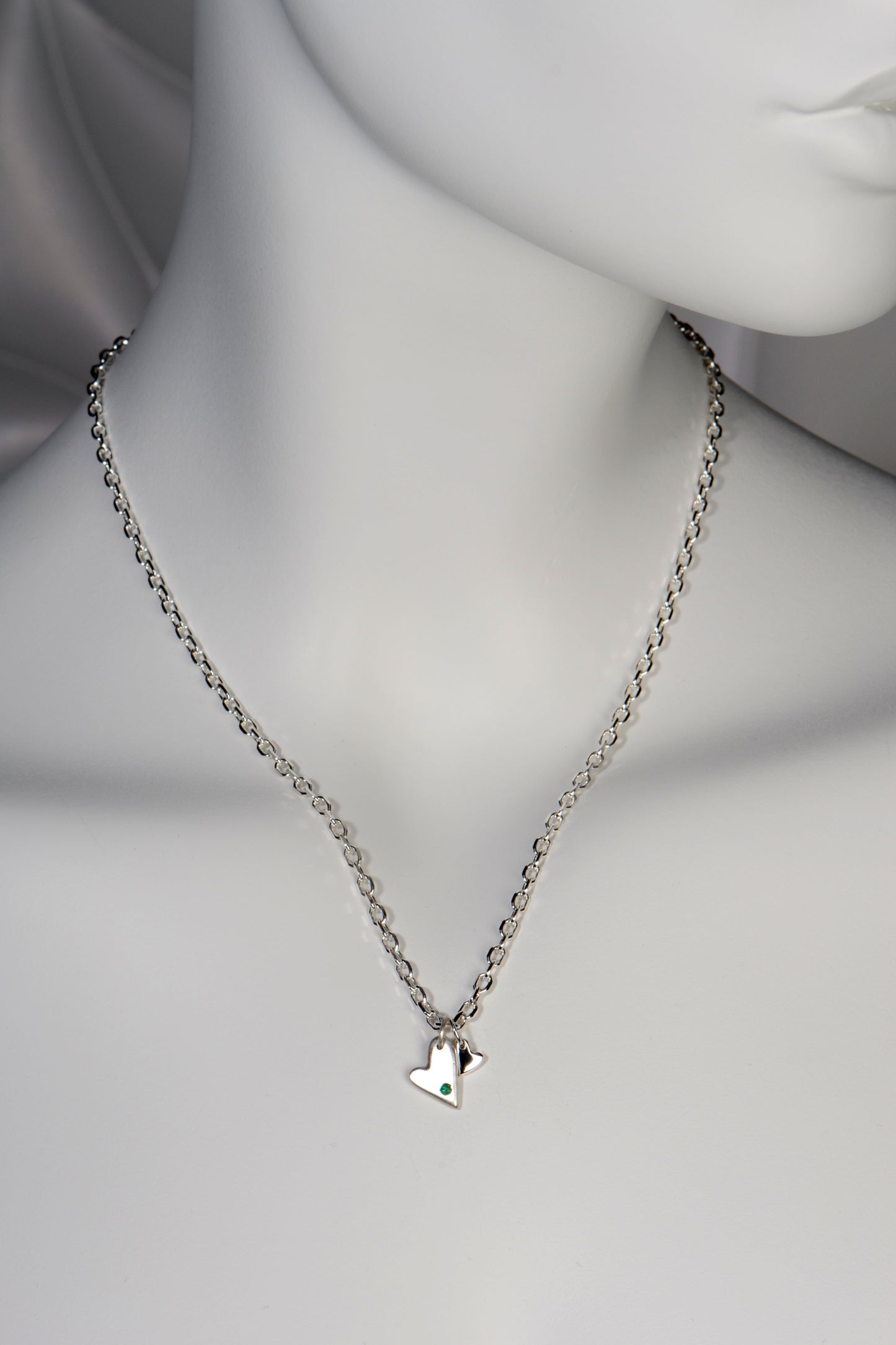 Sterling silver double heart necklace set with emerald displayed on white mannequin to show size and scale