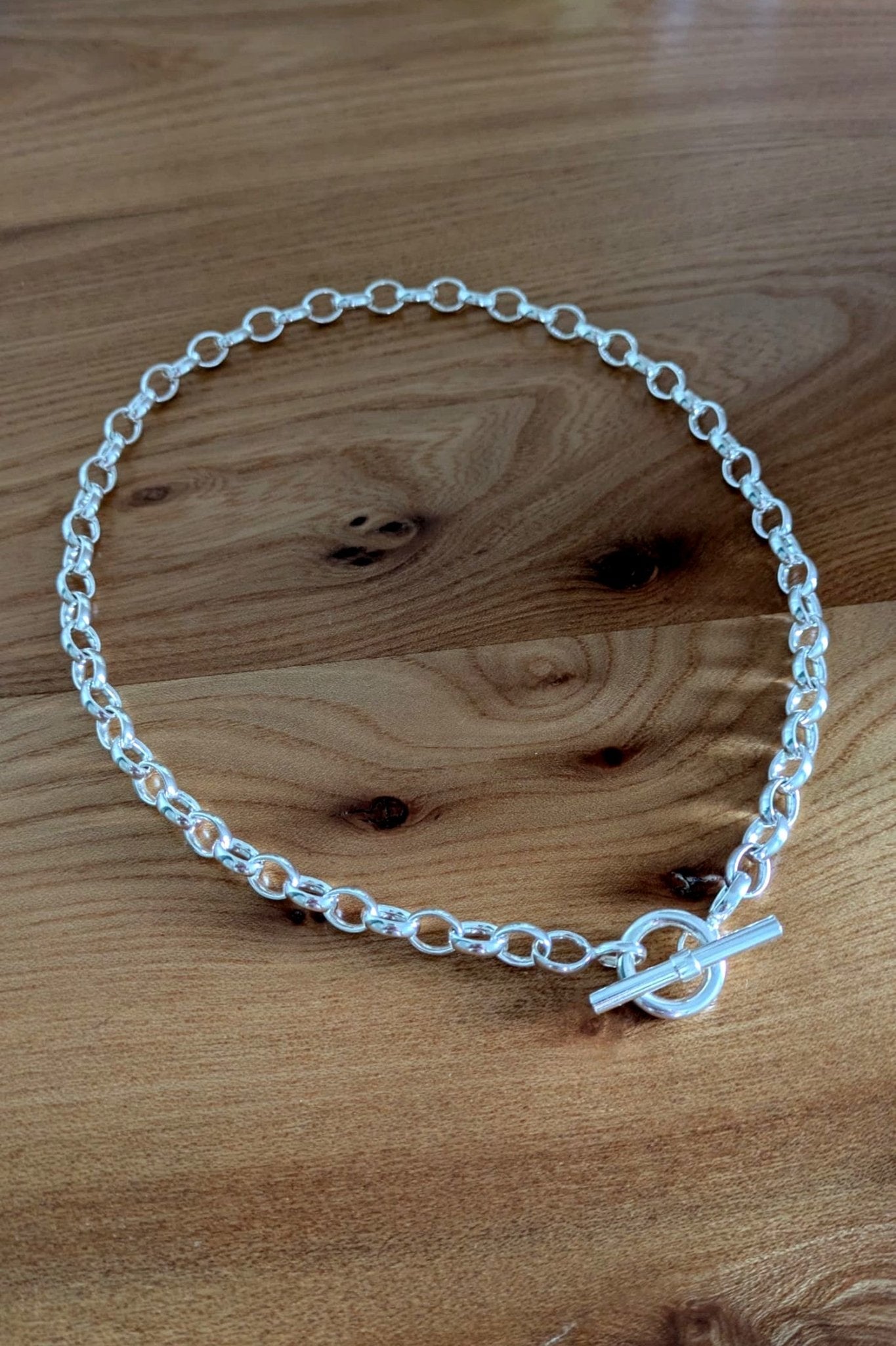 Close-up of sterling silver T-bar necklace on wooden background – durable chain with soldered links