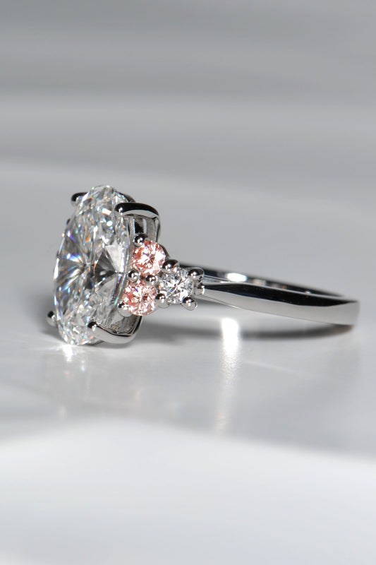 Close-up of Rosé Spark ring showing two pink lab diamonds and one white lab diamond on each side of the central oval stone, forming a white–pink–white sequence.