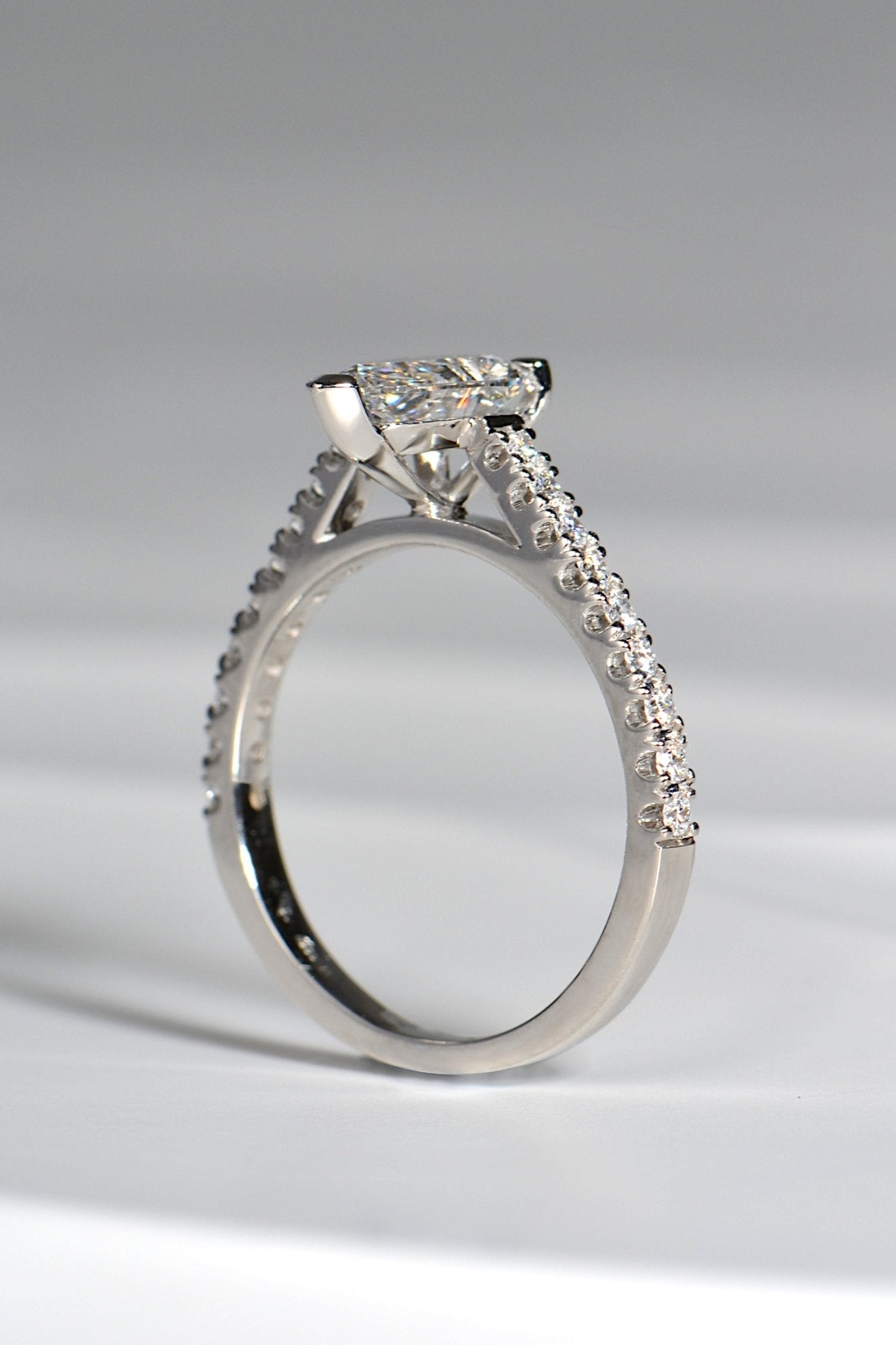 view of side of a pearl cut diamond engagement ring in platinum that has diamonds in the shoulders