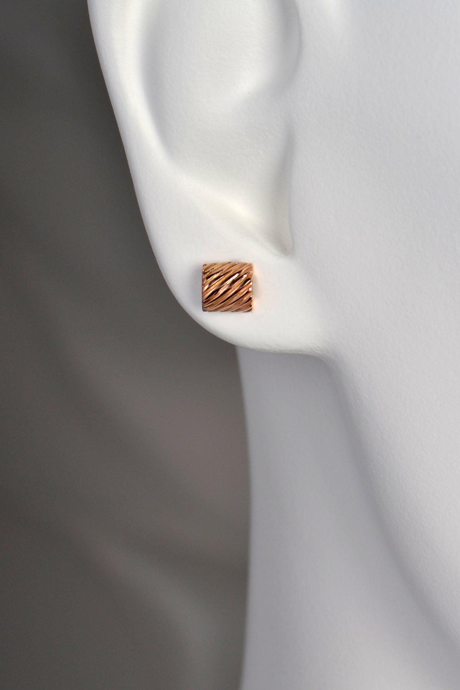 rectangular real rose gold stud earring with texture. The earring sits on the earlobe.