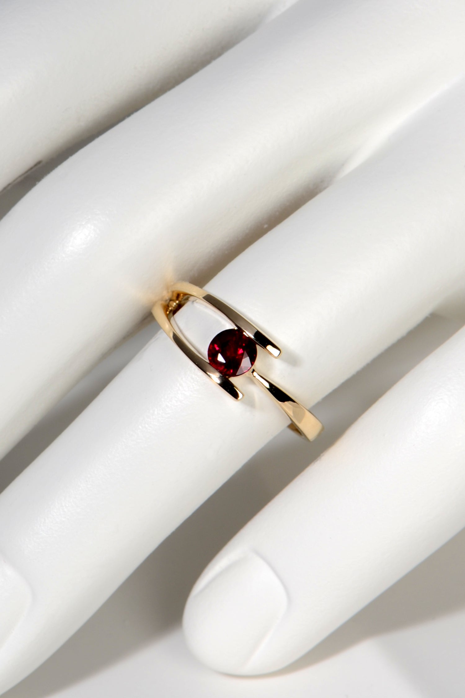 modern yellow gold ring with a round ruby on a mannequin hand