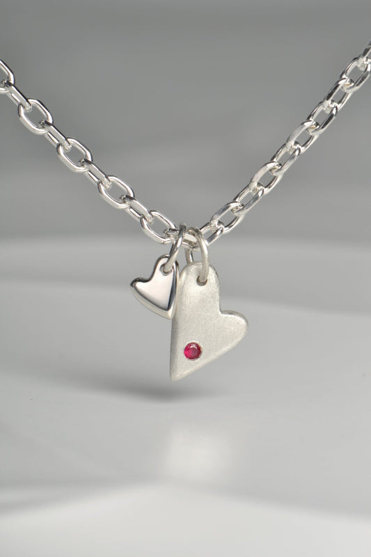 close up of sterling silver double heart necklace set with a ruby displayed on white background from the From The Heart collection by Christine Sadler