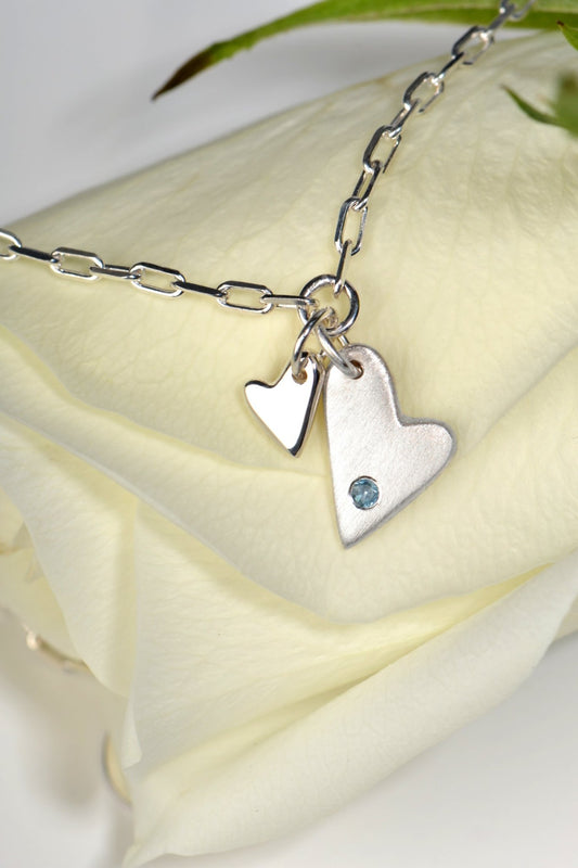 Sterling silver two‑heart bracelet with aquamarine displayed on white rose  from the From The Heart collection by Christine Sadler