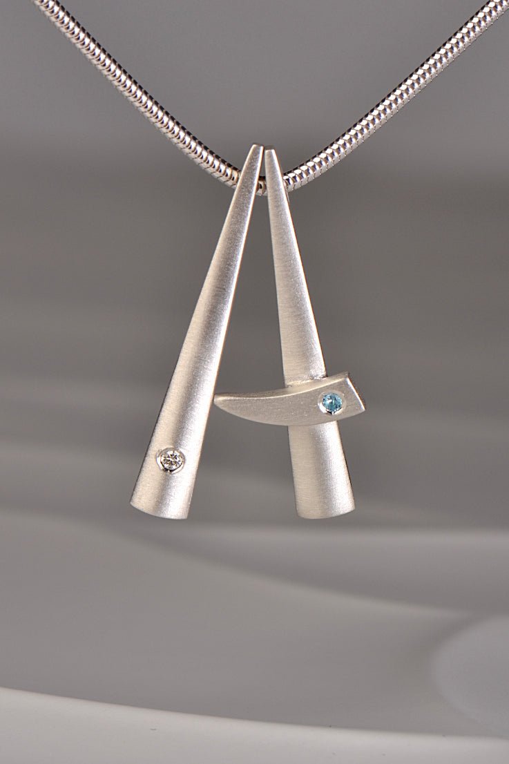 two modern brushed finished silver pendants that stack together , one set with a diamond and one with a blue topaz. This exclusive collection of jewellery is called Cairn and you can stack different gemstones together to mark important moments in your personal journey from Scottish jewellery designer Christine Sadler