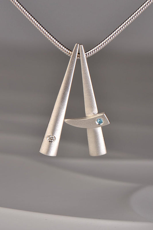 two modern brushed finished silver pendants that stack together , one set with a diamond and one with a blue topaz. This exclusive collection of jewellery is called Cairn and you can stack different gemstones together to mark important moments in your personal journey from Scottish jewellery designer Christine Sadler