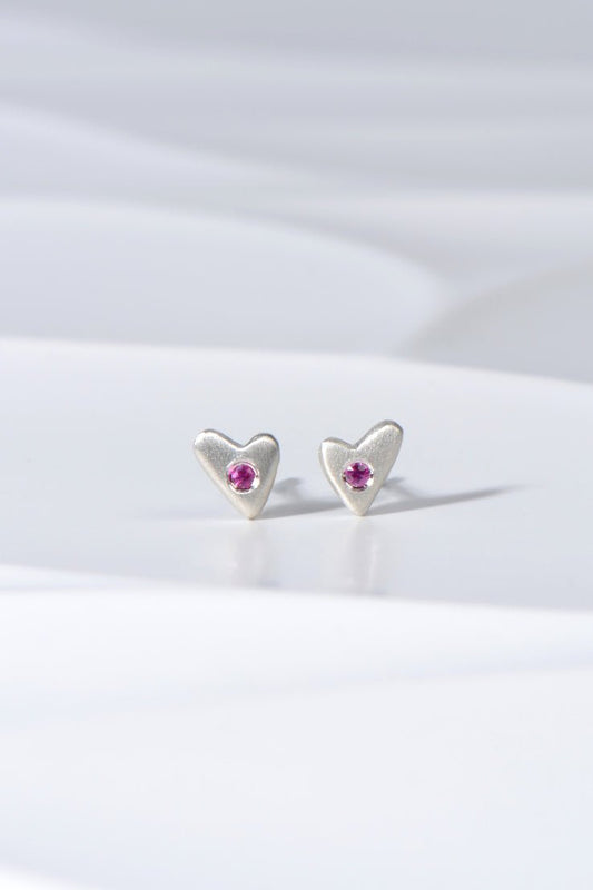 Small matt silver heart stud earrings set with pink sapphires displayed on white background from the From The Heart collection by Christine Sadler