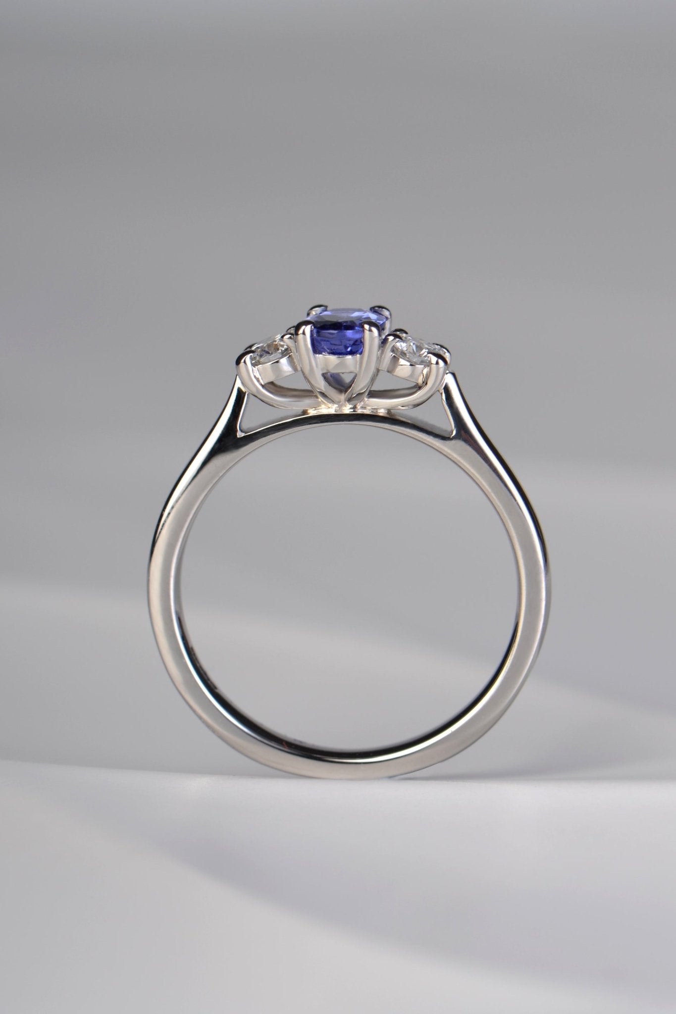 Three stone tanzanite and diamond platinum engagement ring with stones raised up so that it will sit perfcctly next to a straight wedding ring. This ring is made in the UK