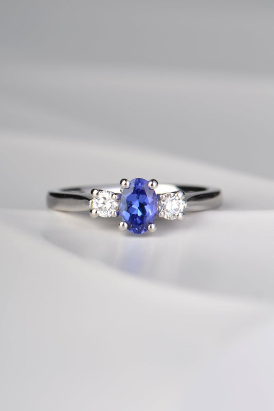 stunning oval cut intense blue tanzanite engagement ring set with two round diamonds, one on either side of the tanzanite. Each stone is held by four claws and it is made in platinum.