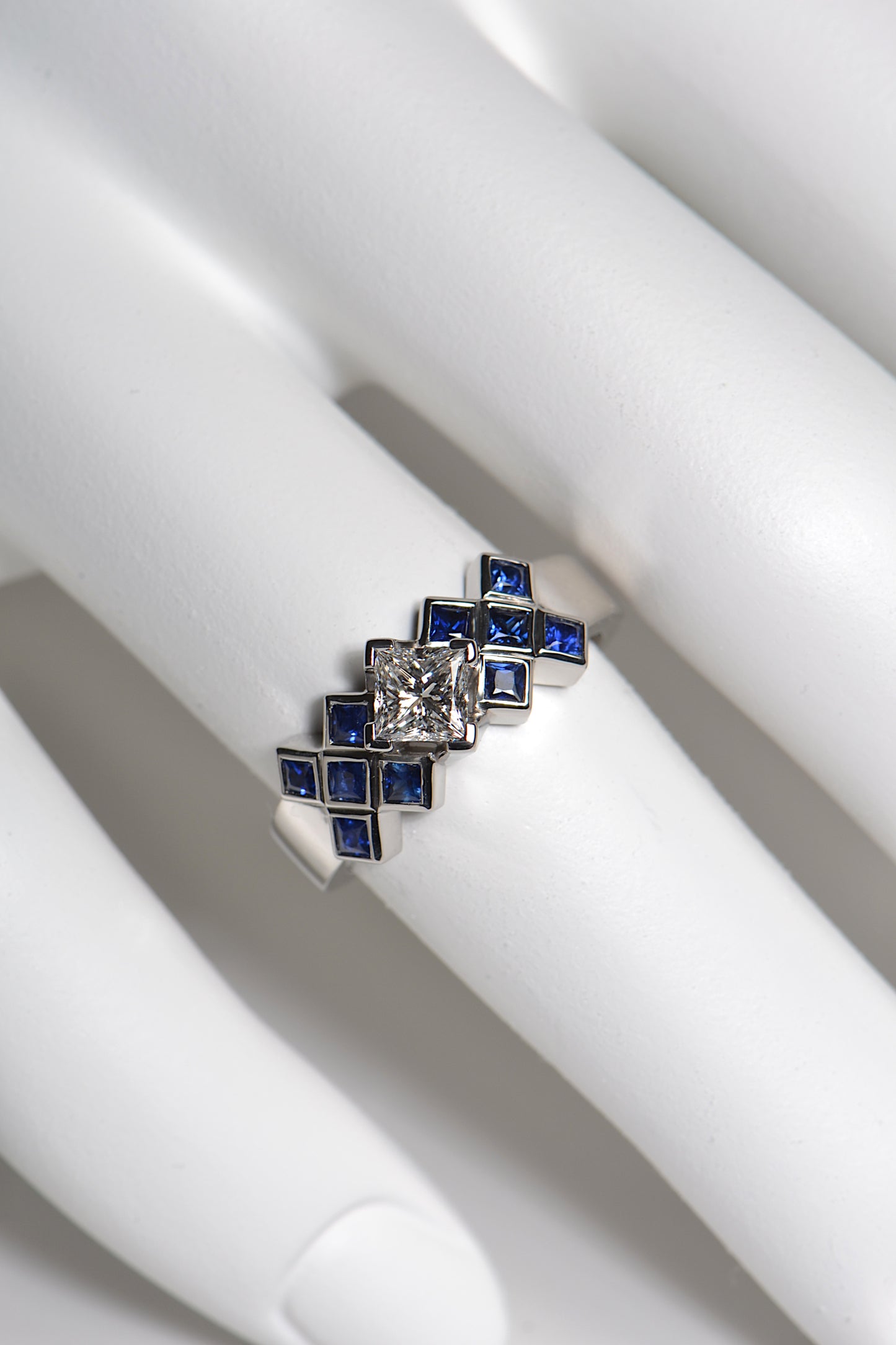 The tartan ring is set with a central 0.53ct princess cut diamond above a chequered pattern of 2mm blue sapphires . The platinum ring is 7.7mm wide at the front so it is a substantial statement engagement ring. This unusual Scottish diamond ring is unmistakably scottish.