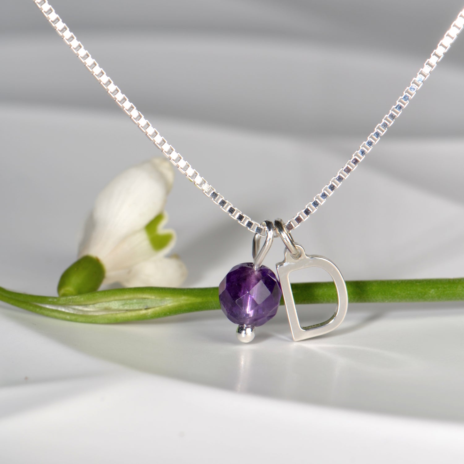silver initial pendant with a faceted round amethyst that hangs next to it on a silver box chain