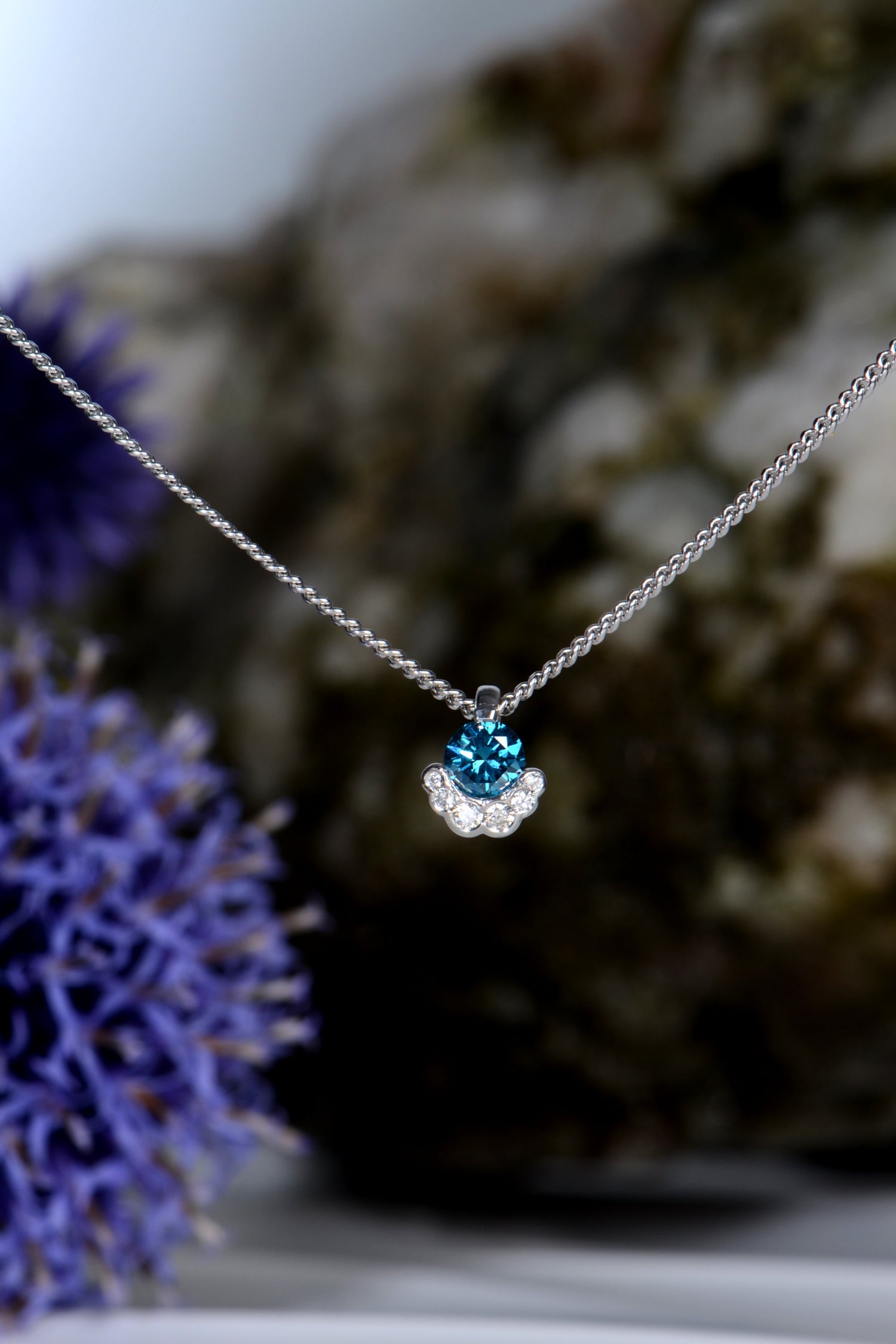 scottish designer platinum diamond necklace by Christine Sadler set with a blue diamond surrounds at the bottom with small white diamonds.