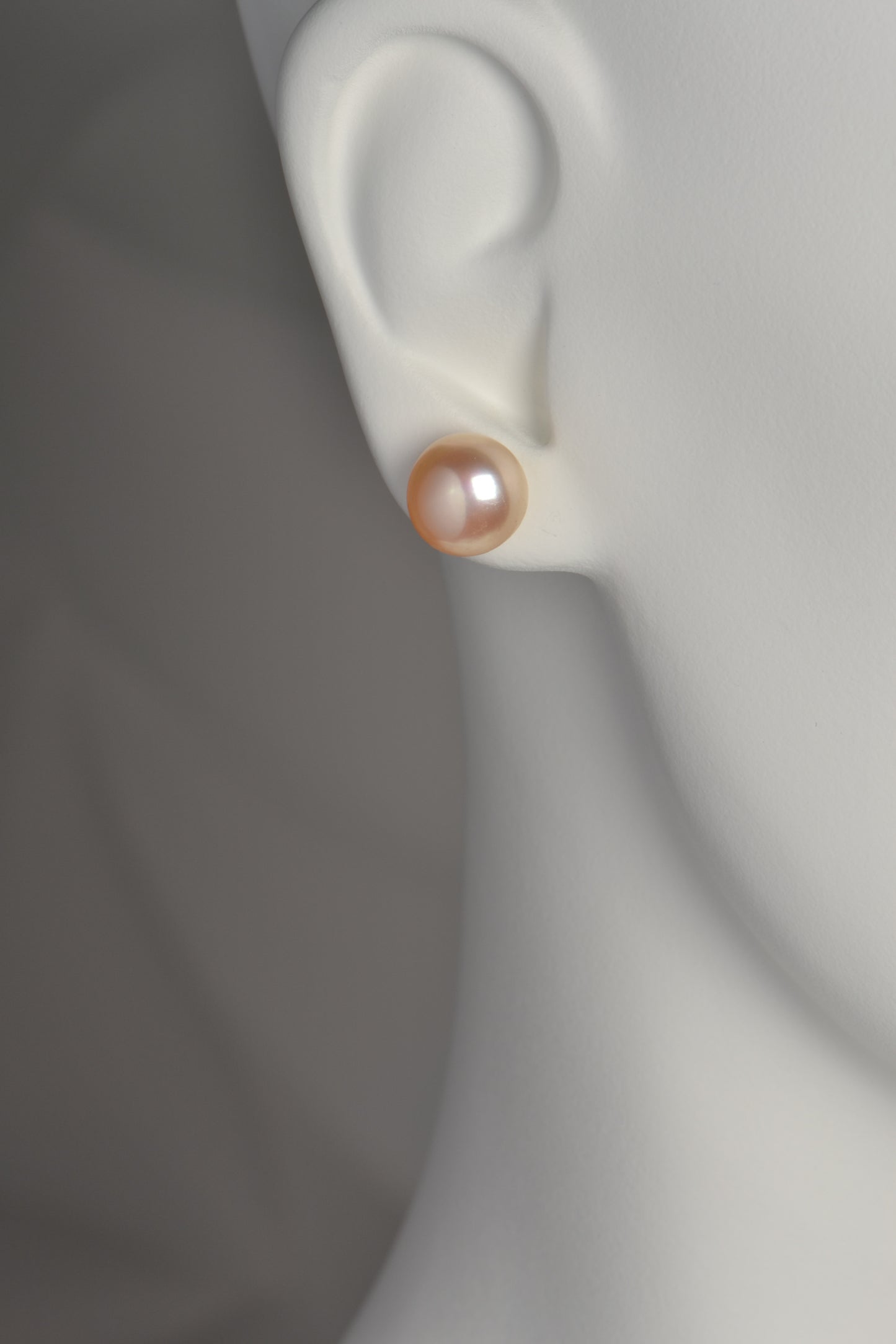 large peach pearl earrings photographed in the earlobe. They cover most of the lobe entirely.