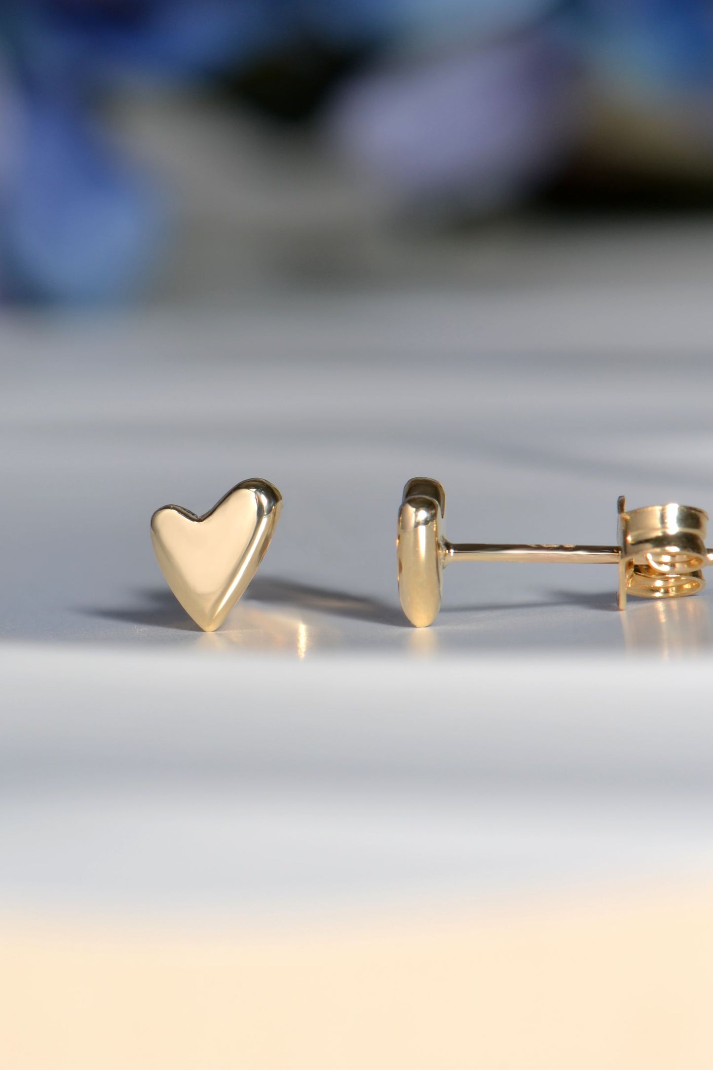 Gold heart-shaped earrings on a light gray surface with a blurred background
