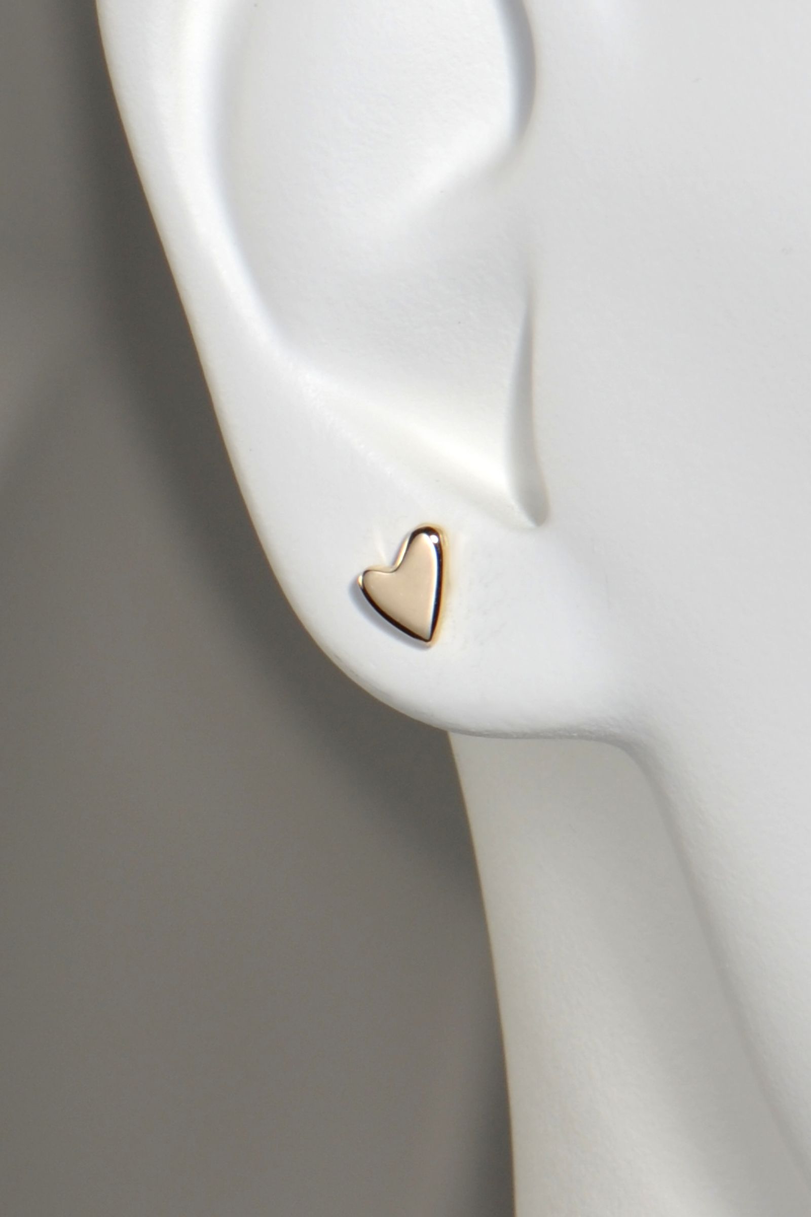 Gold heart-shaped earring on a white mannequin ear