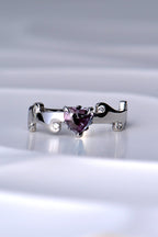 real Alexandrite heart cut gemstone platinum ring in a magenta pink colour under incandescent light, green in daylight, in a fire ring design with tiny flames around the heart cut gemstone and in the band wihich also has six round brilliant cut diamonds