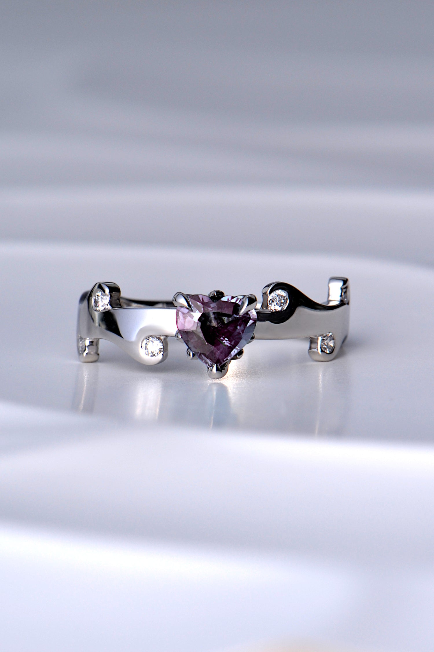 real Alexandrite heart cut gemstone platinum ring in a magenta pink colour under incandescent light, green in daylight, in a fire ring design with tiny flames around the heart cut gemstone and in the band wihich also has six round brilliant cut diamonds