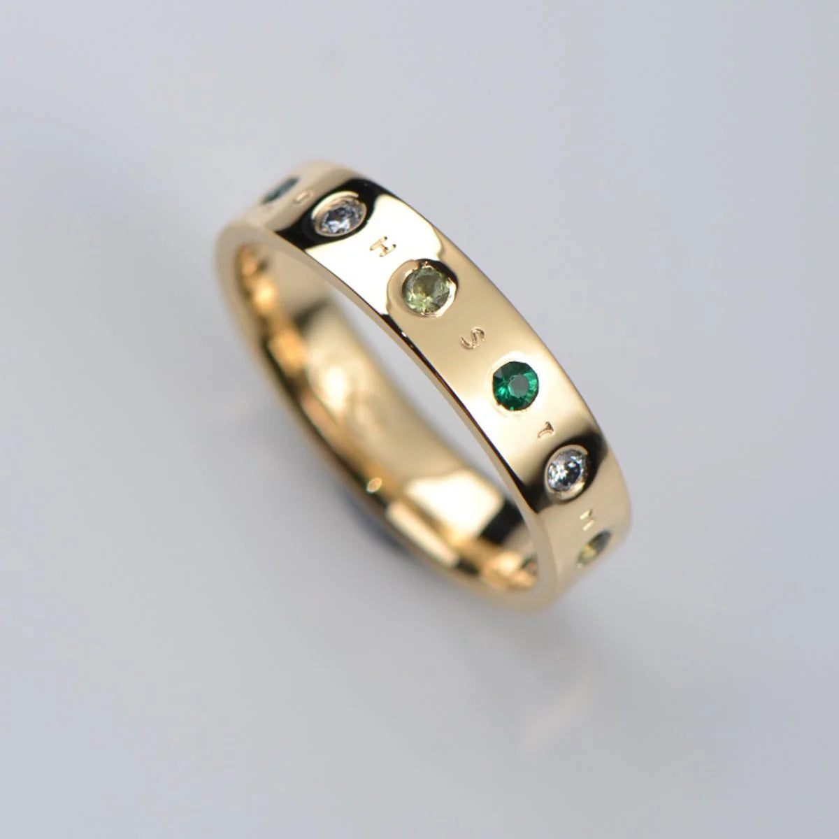 Gold ring with embedded green gemstones that hide a secret message - Christine Sadler Enigma ring design
