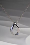 Modern polished sterling silver pendant in a twisted ribbon design that forms a droplet shape with a space in the middle. Like a teardrop shape. This necklace is by Jorge Revilla