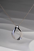 Modern polished sterling silver pendant in a twisted ribbon design that forms a droplet shape with a space in the middle. Like a teardrop shape. This necklace is by Jorge Revilla