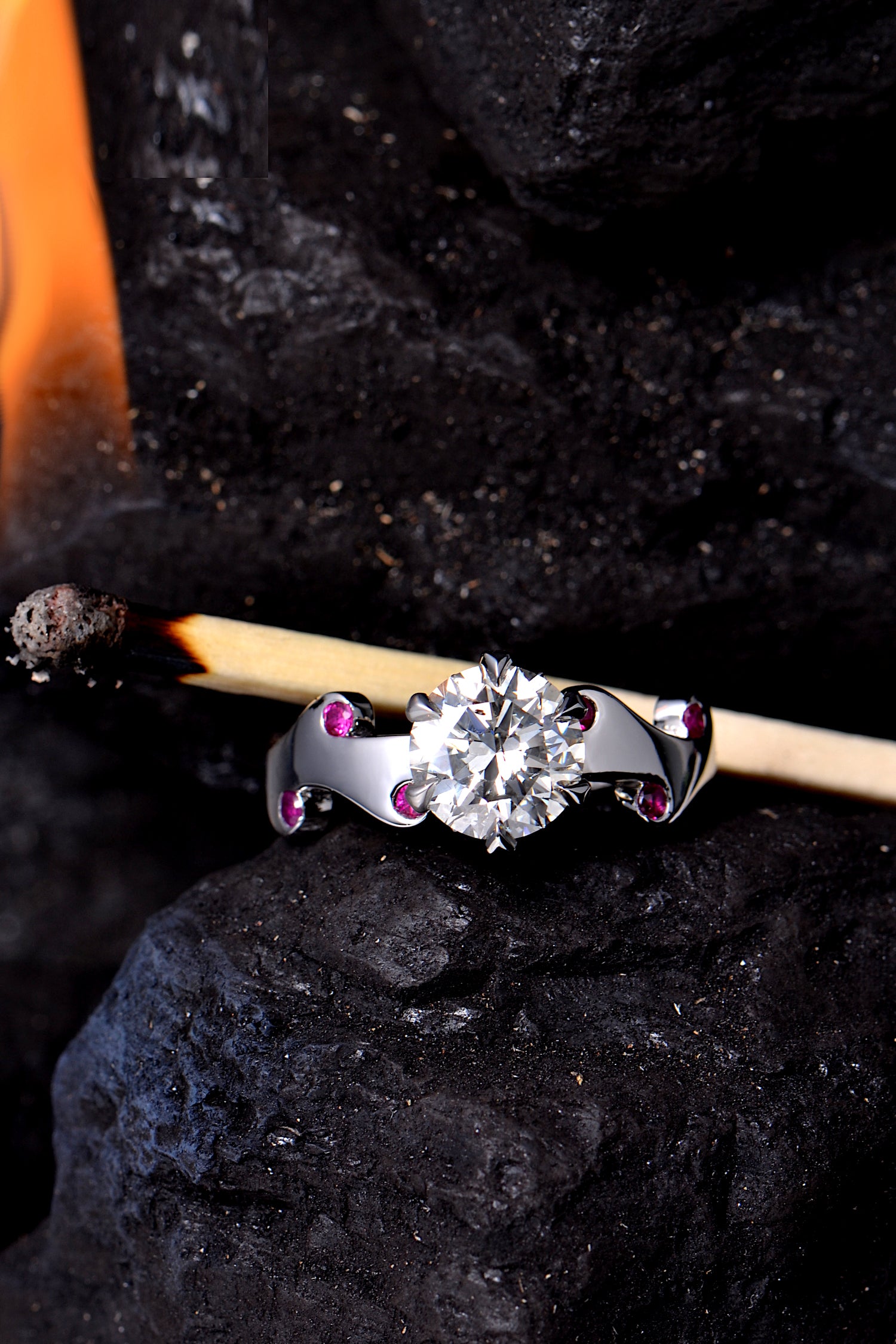 designer diamond and ruby platinum ring with romantic fire design by Christine Sadler photographed on coal with a lighted match