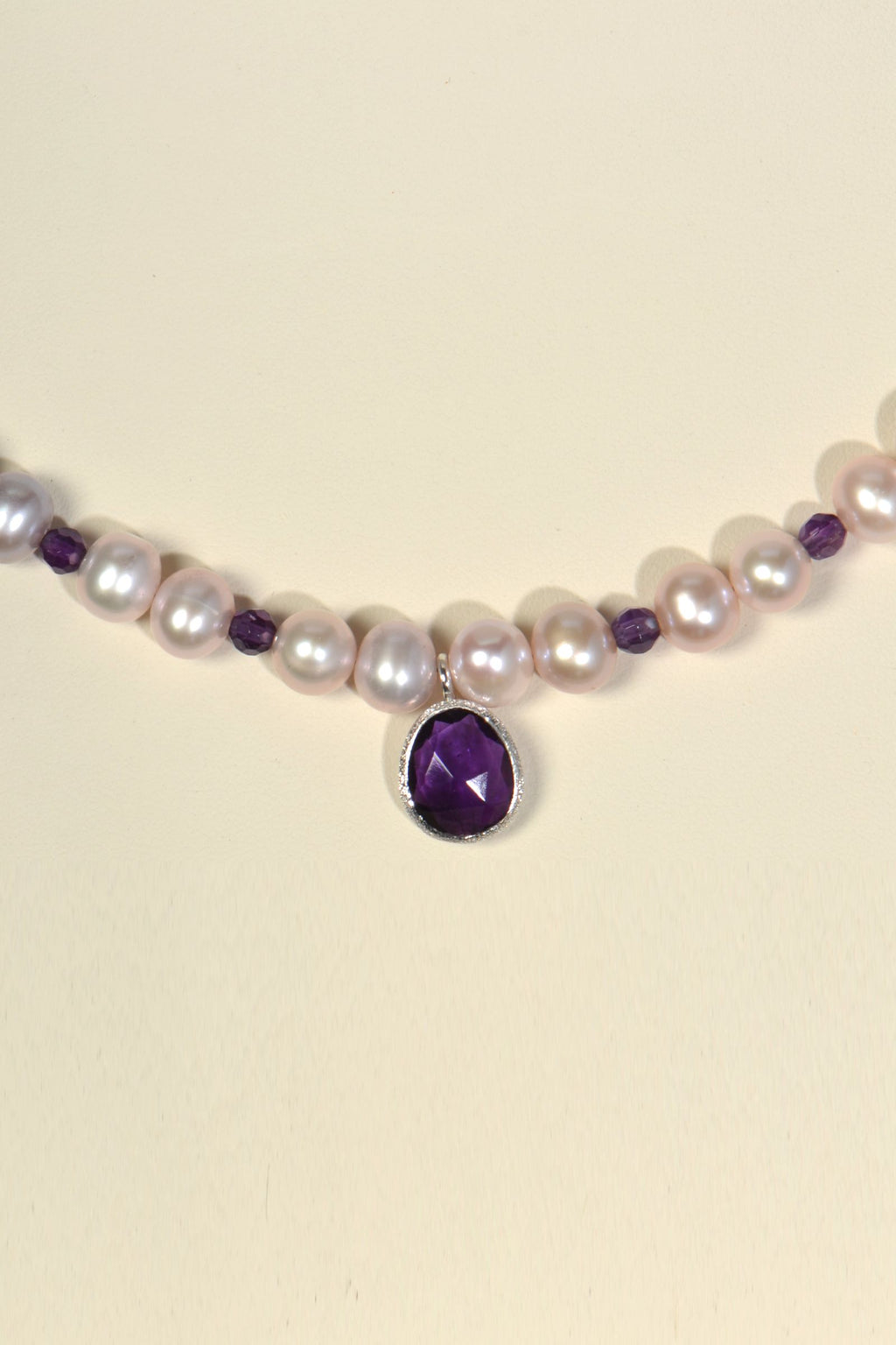 close up detail of amethyst pendant at font of pink pearl necklace