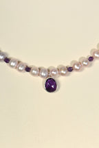 close up detail of amethyst pendant at font of pink pearl necklace