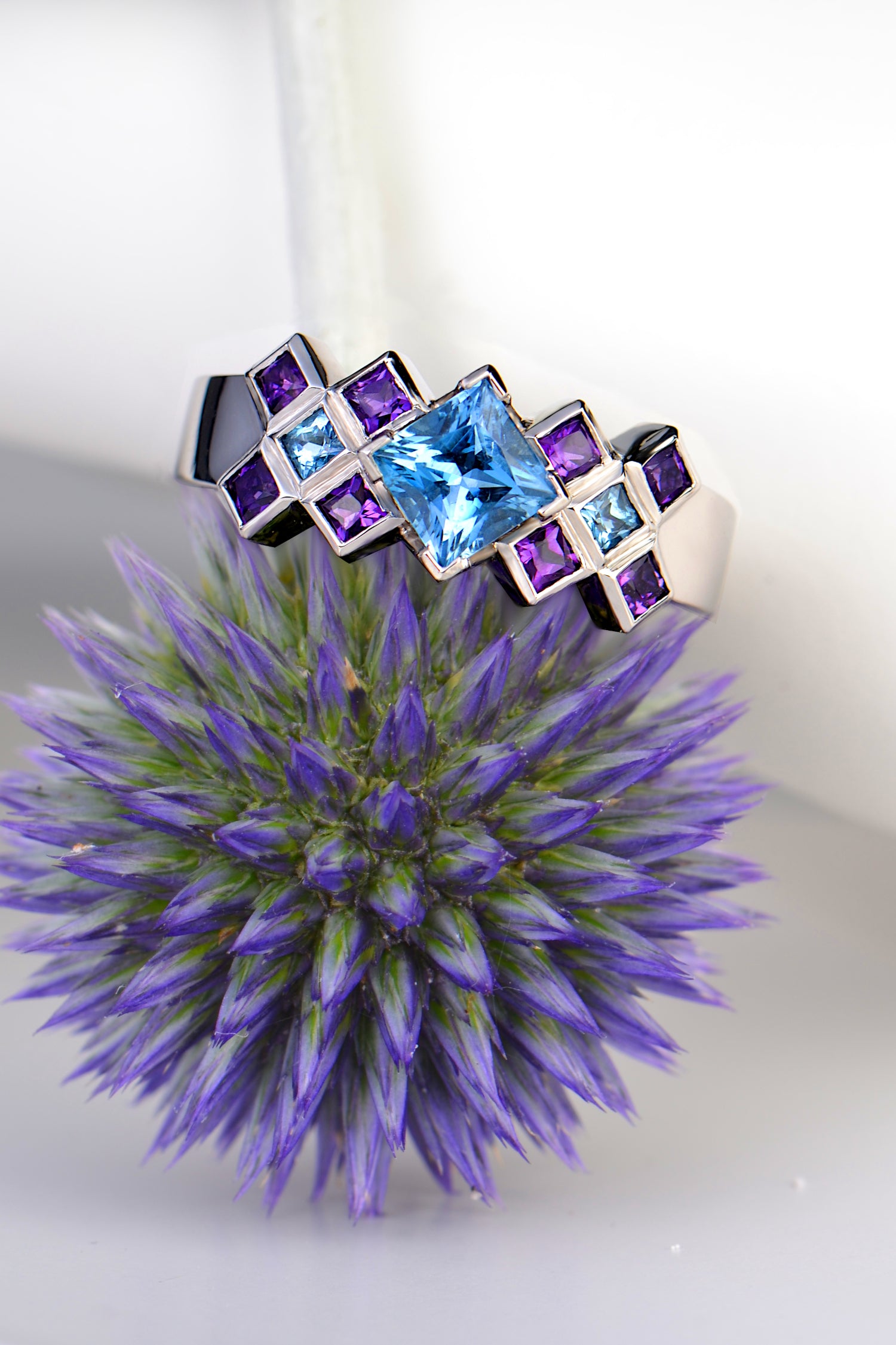 scottish platinum engagement ring with aquamarine and amethysts inspired by tartan photographed  sitting on top of a thistle