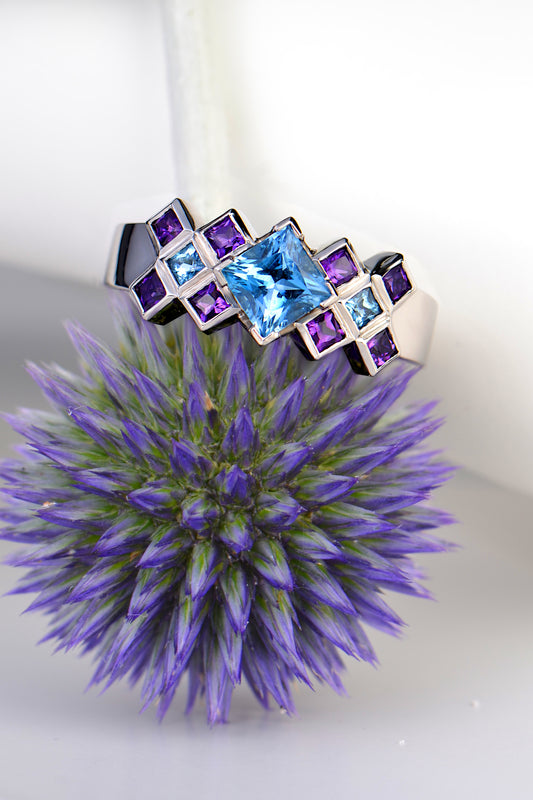 scottish platinum engagement ring with aquamarine and amethysts inspired by tartan photographed  sitting on top of a thistle