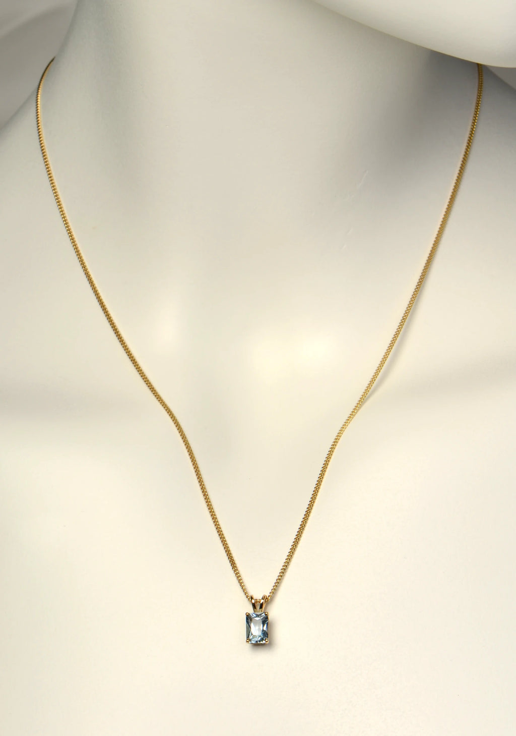 British made 9ct yellow gold radiant cut aquamarine pendant on 9ct yellow gold curb chain on a white mannequin to show length and scale - Christine Sadler
