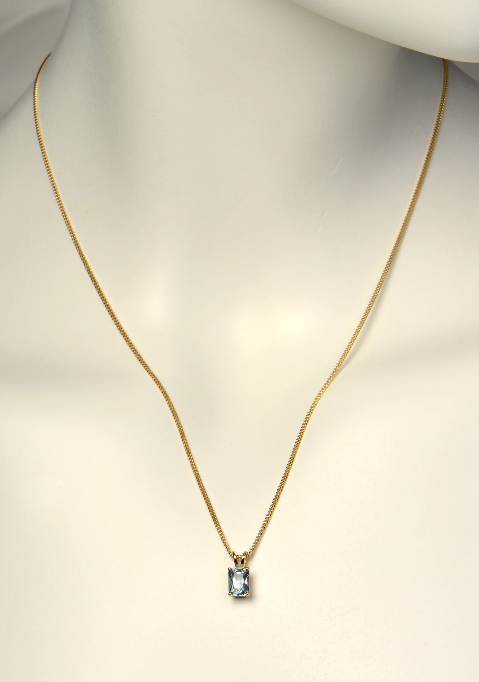 British made 9ct yellow gold radiant cut aquamarine pendant on 9ct yellow gold curb chain on a white mannequin to show length and scale - Christine Sadler