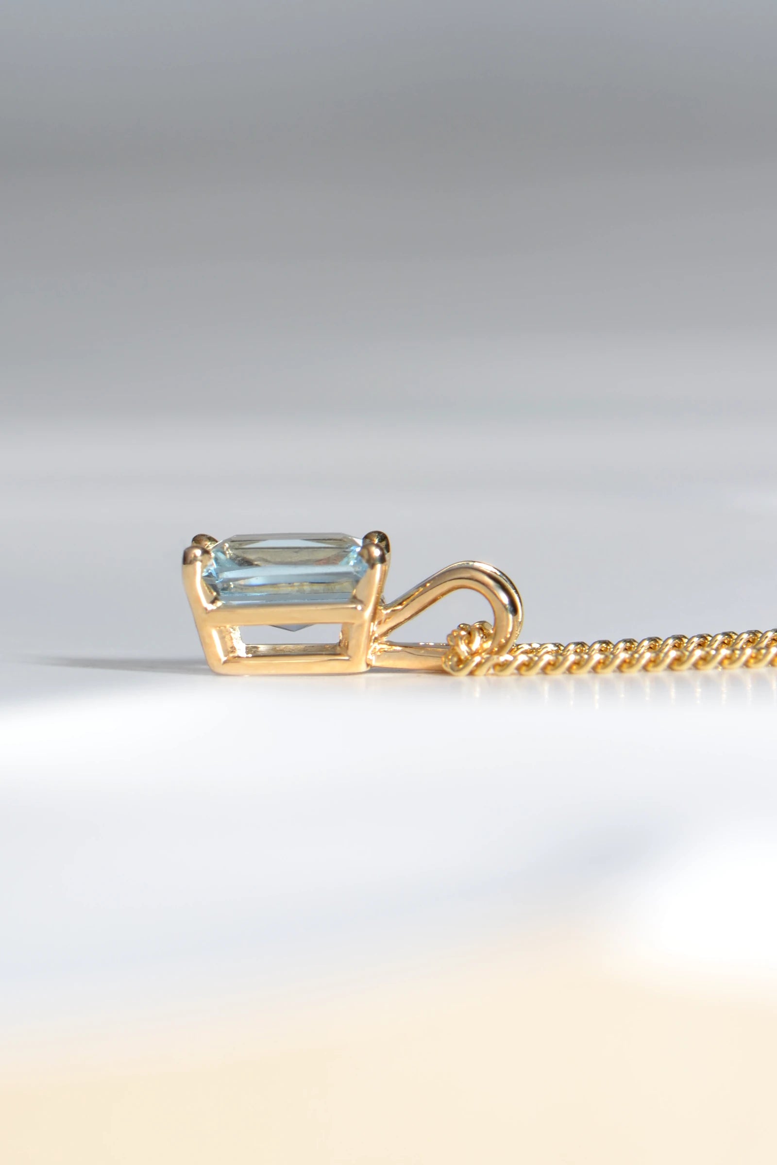 side view of 9ct yellow gold pendant set with a rectangular radiant cut aquamarine in a four claw setting with a double loop bail - Christine Sadler