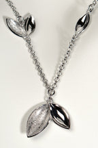 modern silver charm necklace with concave seed like shapes in highly polished silver and modern textured finishes. Called The Promise, a tree is planted for each one of these necklaces sold by Christine Sadler
