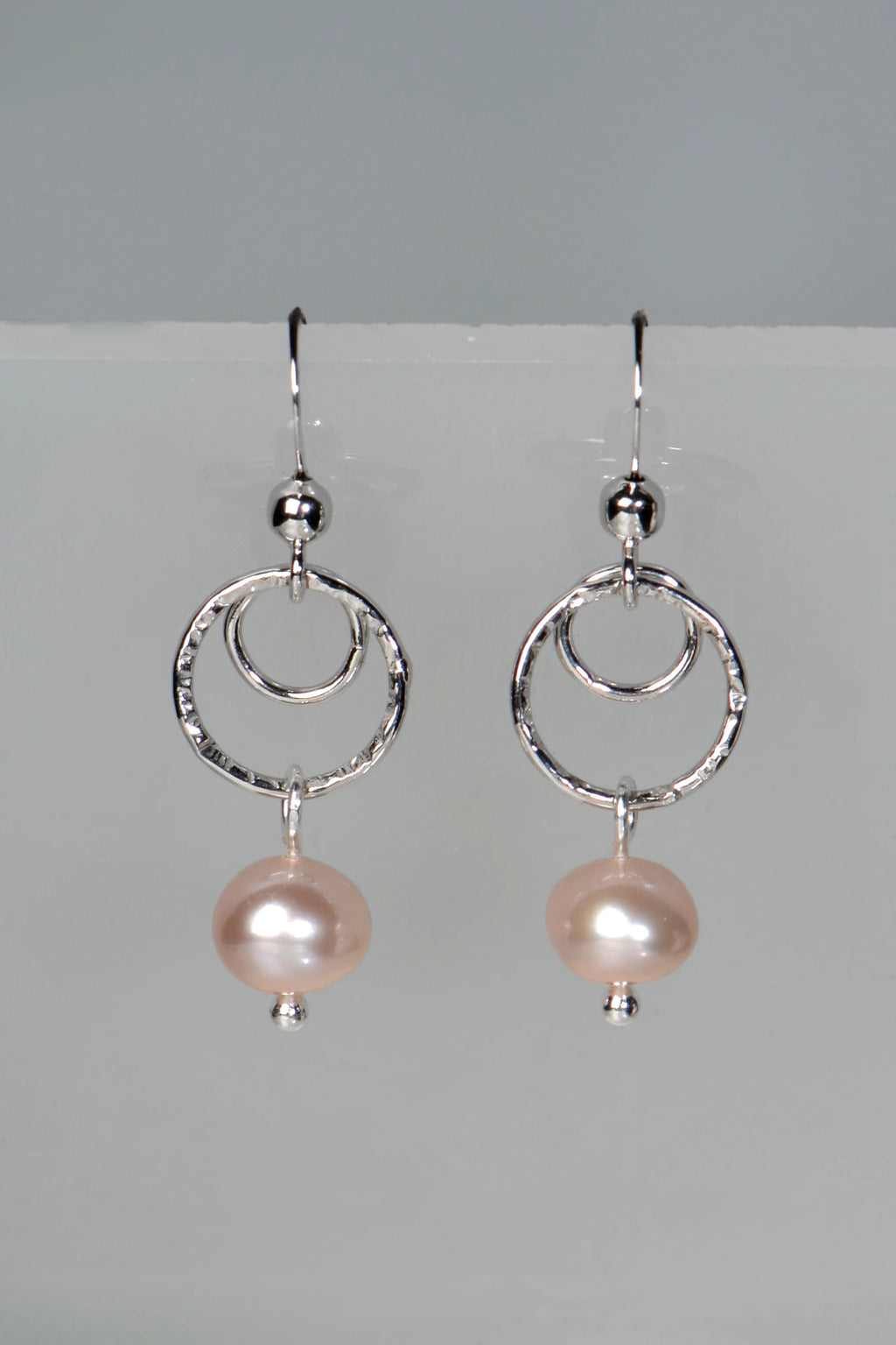 Handmade sterling silver circle earrings with pink cultured on a gray background
