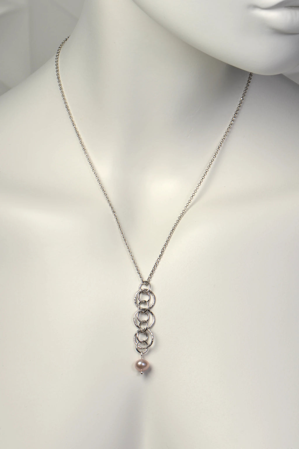 Sterling silver interlocking circle pendant with a pink cultured pearl at the bottom on a mannequin against a white background