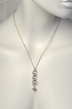Sterling silver interlocking circle pendant with a pink cultured pearl at the bottom on a mannequin against a white background