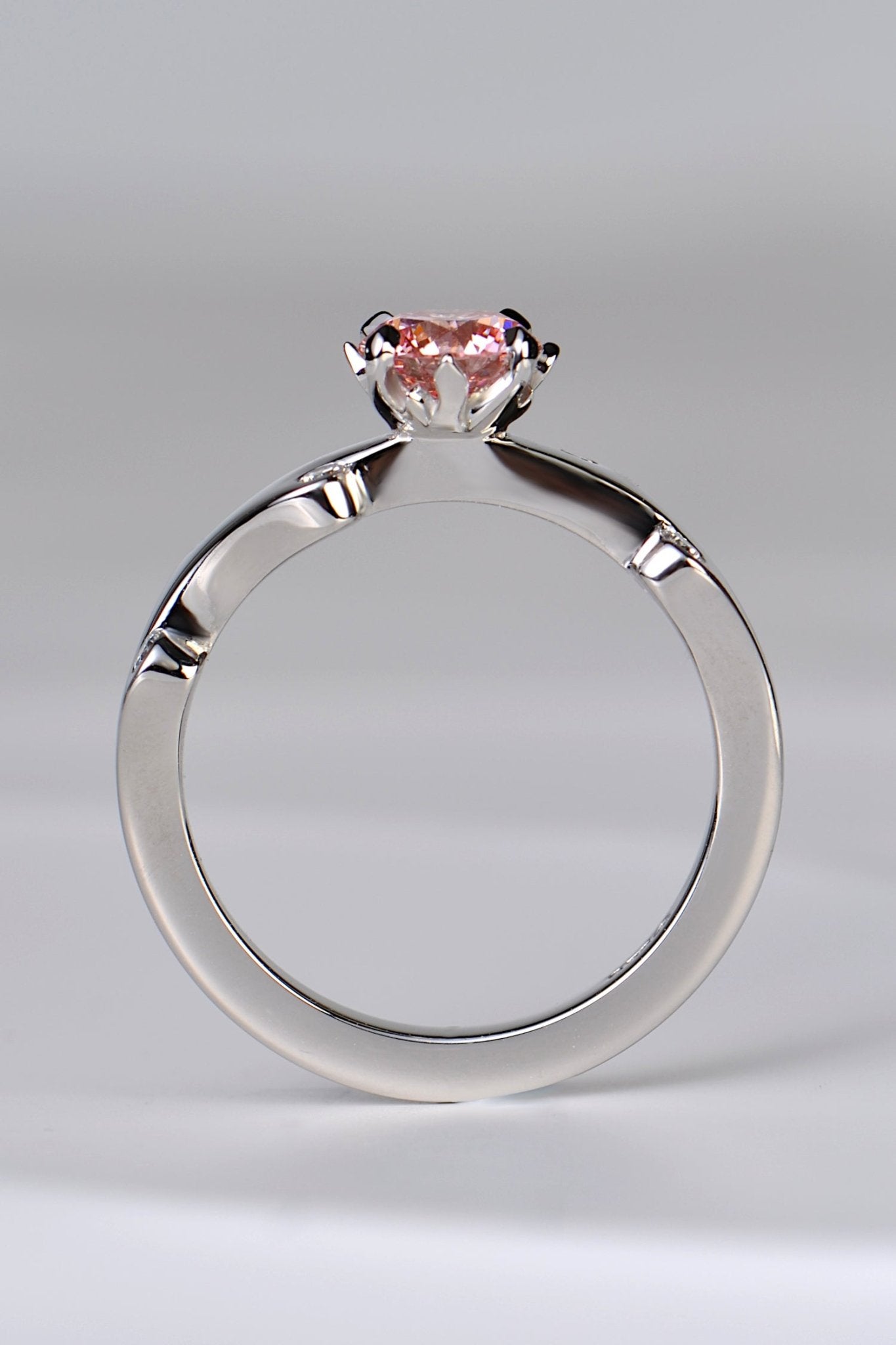 A platinum engagement ring set with a large round pink lab diamond in rose pink shade. The diamond is held in a setting that looks like tiny flames are surrounding it. A unique and special diamond ring design by jewellery designer Christine Sadler.