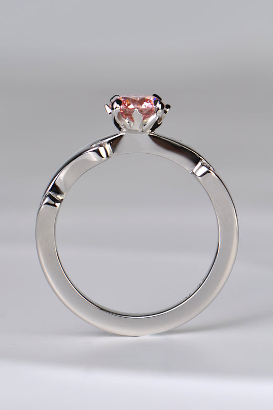 A platinum engagement ring set with a large round pink lab diamond in rose pink shade. The diamond is held in a setting that looks like tiny flames are surrounding it. A unique and special diamond ring design by jewellery designer Christine Sadler.
