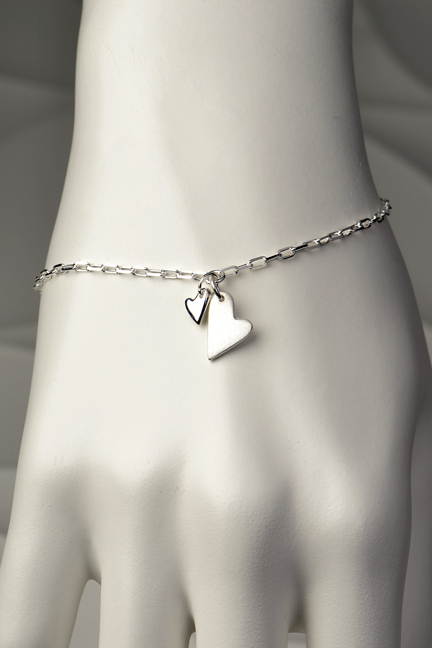 Two-heart silver bracelet worn on wrist, showing elegant modern design and meaningful pairing of brushed and polished hearts