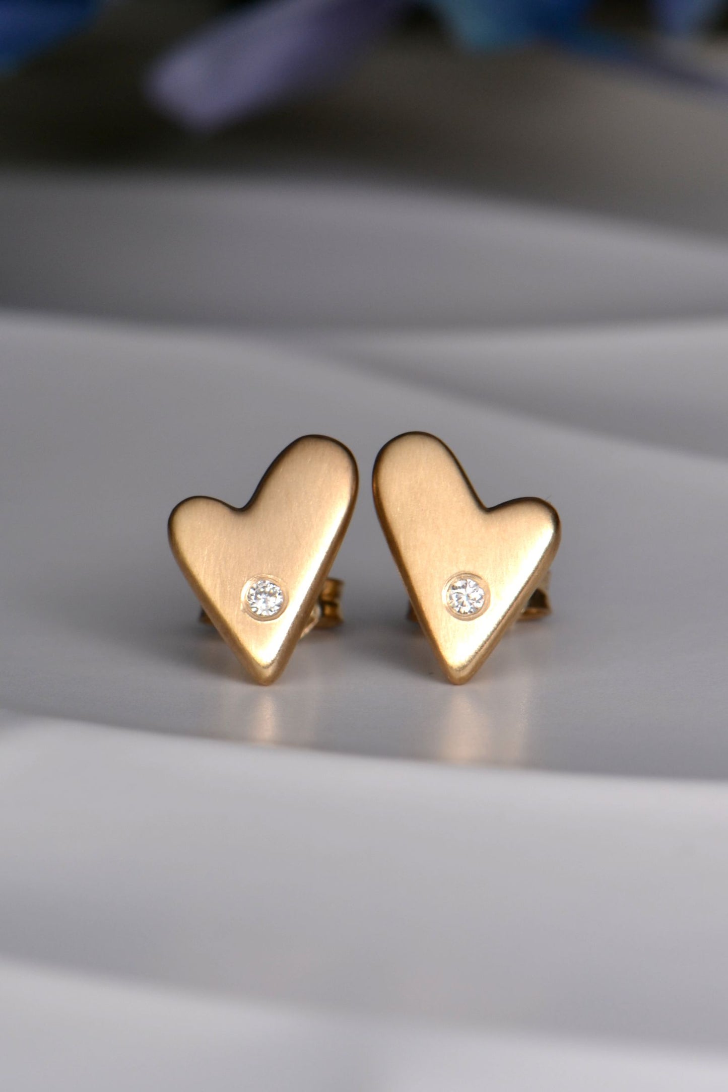 Gold heart-shaped earrings with small diamonds on a light gray surface.