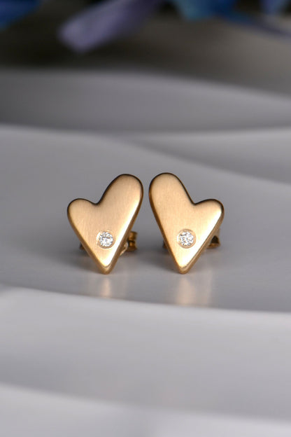 Gold heart-shaped earrings with small diamonds on a light gray surface.