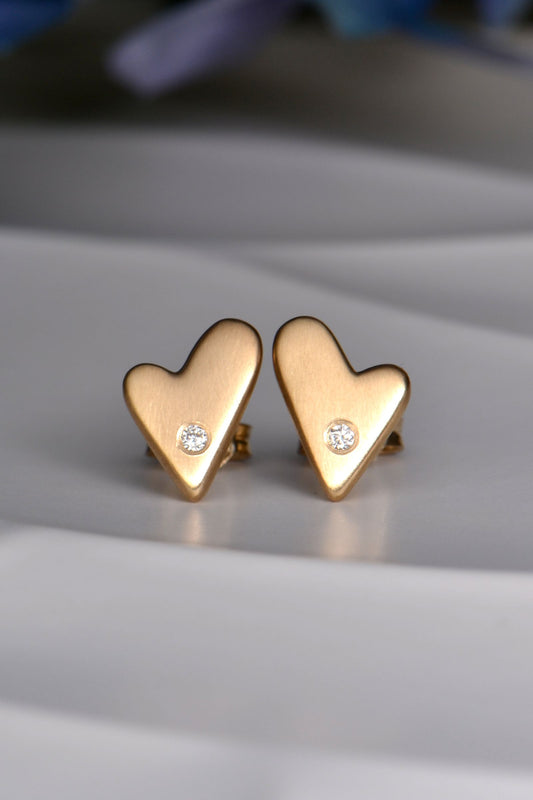 Gold heart-shaped earrings with small diamonds on a light gray surface.