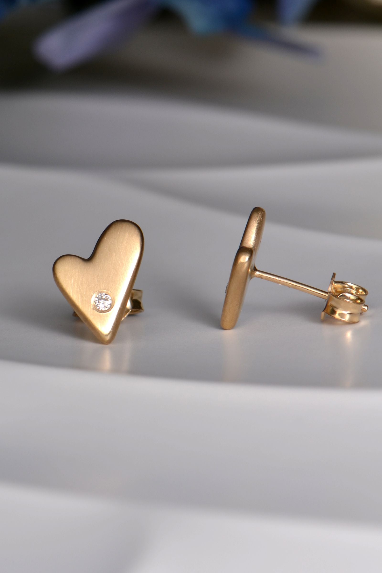 Gold heart-shaped earrings on a light gray surface, turned to show the post and butterfly earring fitting